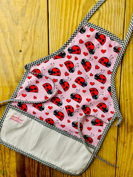 Amanda Bright Designs Children's ladybug apron pink with red and black ladybugs and black checkered trim
