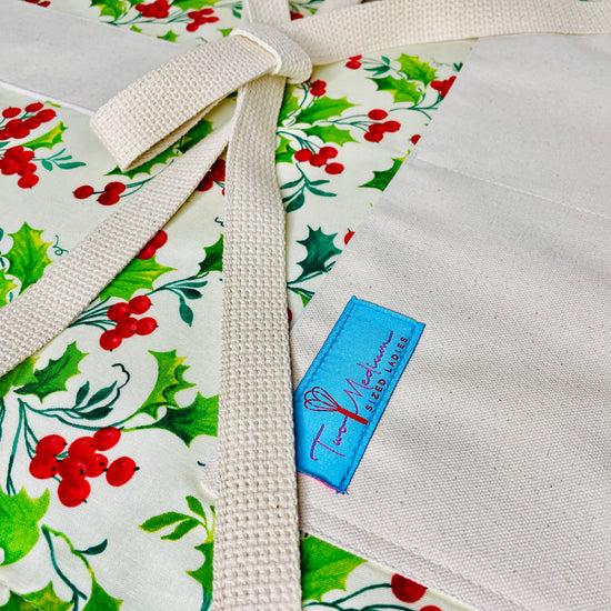 Two Medium Sized Ladies winter hollyberry apron with cotton strings close up view of winter wonderland holly tree