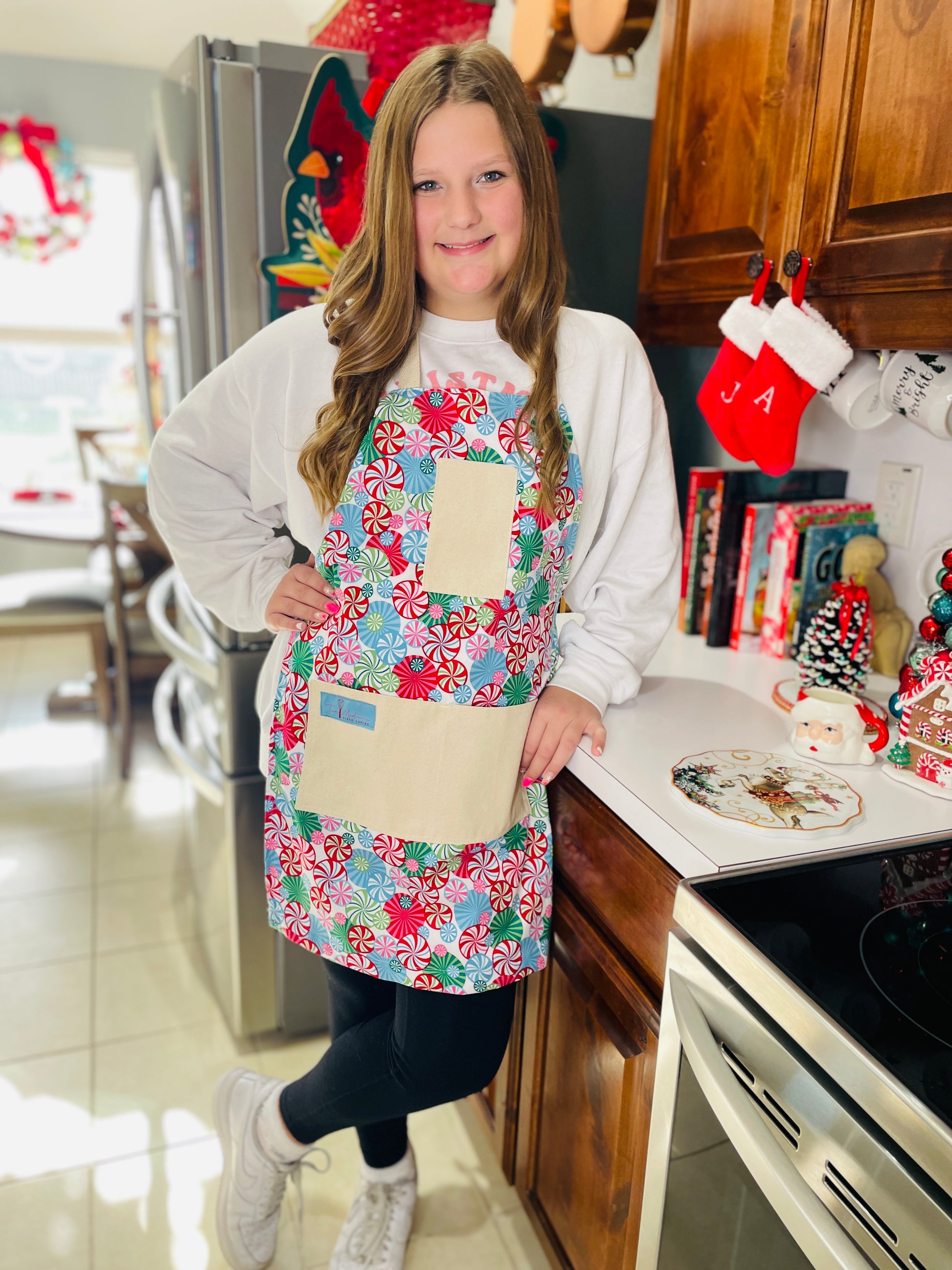 Two Medium Sized Ladies peppermint lane candy land Christmas apron on preteen teenager baking cookies
