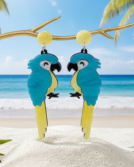 Amanda Bright Designs Blue and yellow parrot acrylic earrings on a branch with a beach background