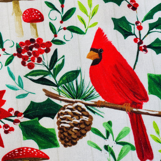 Amanda Bright Designs festive Christmas print apron featuring red cardinals, poinsettias, holly leaves, pinecones, and red mushrooms
