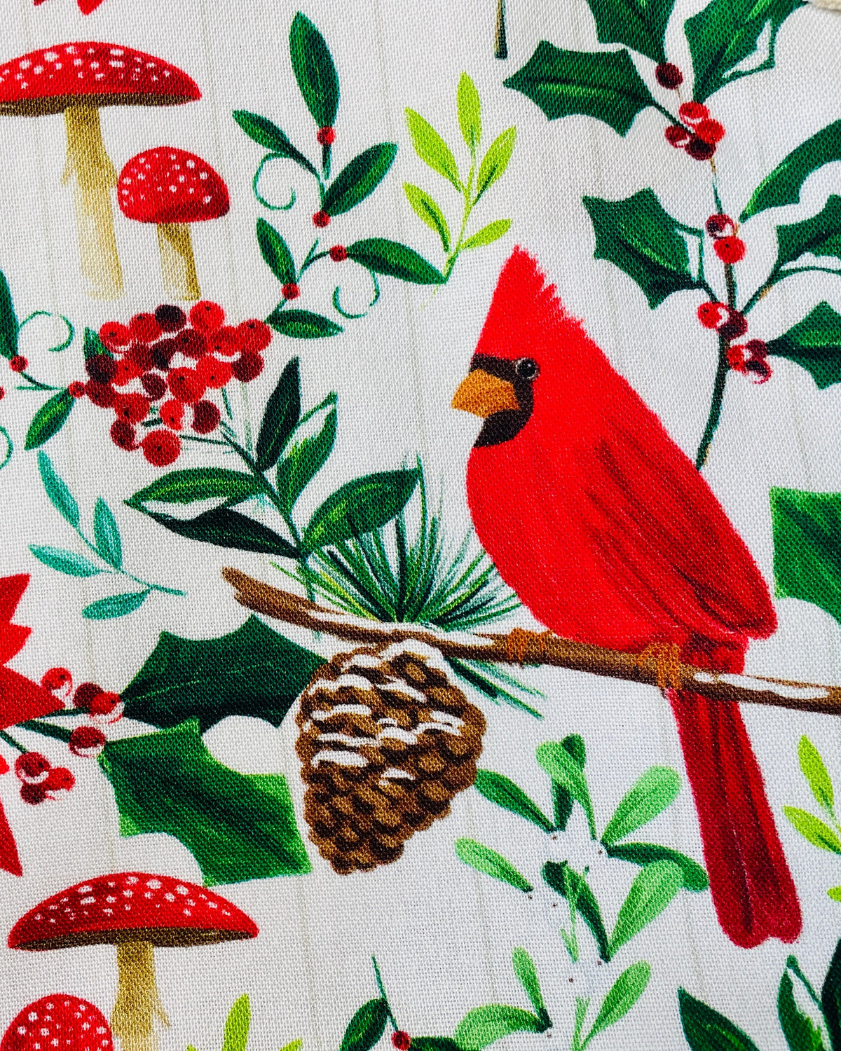Amanda Bright Designs festive Christmas print apron featuring red cardinals, poinsettias, holly leaves, pinecones, and red mushrooms