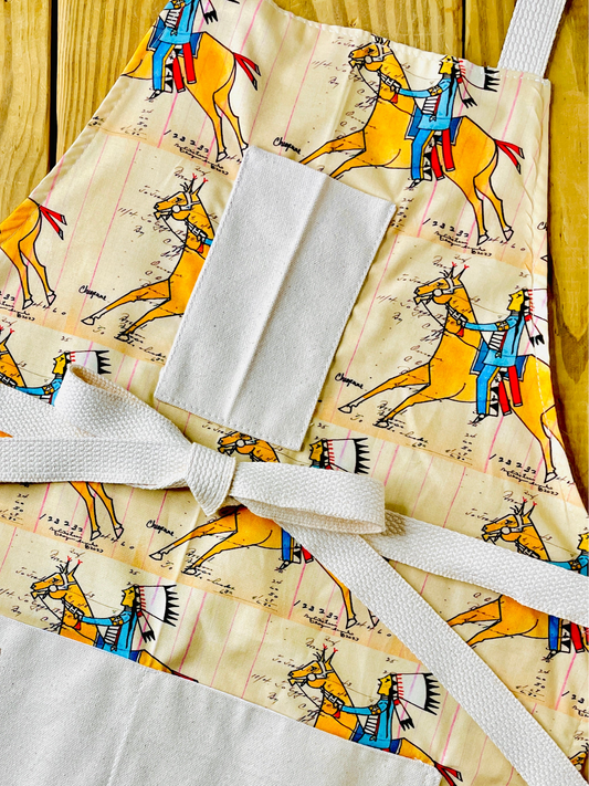 Amanda Bright Designs cheyenne warrior indian chief apron with cream background and a repeating print of indian on horseback wearing red and blue with his headdress on and figural marks on the pattern