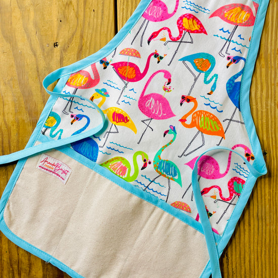 Amanda Bright Designs children’s kitchen apron with a colorful flamingo print on a white background, featuring Tiffany blue trim and natural canvas front pockets