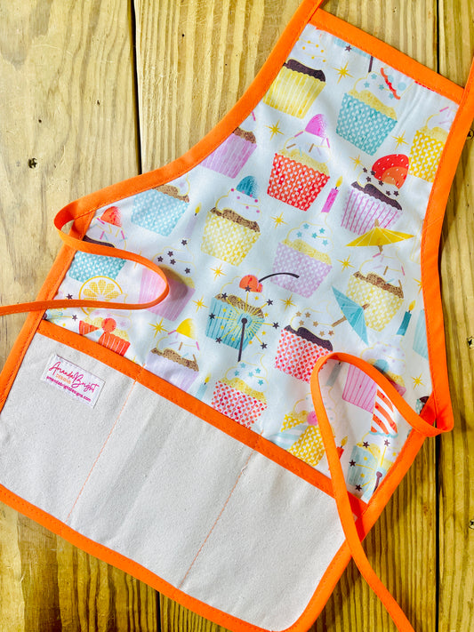 Amanda bright designs children’s birthday party apron featuring colorful cupcakes with frosting decorations fruit for birthday celebrations