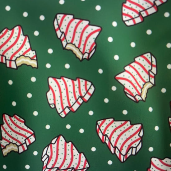 Our Couture Christmas Tree Cakes Holiday Apron features the iconic striped Little Debbie Christmas Tree Cake with a bite out of it on a green polkadot backdrop Amanda Bright Designs