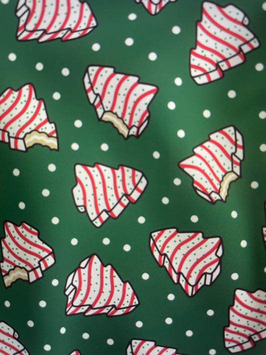 Our Couture Christmas Tree Cakes Holiday Apron features the iconic striped Little Debbie Christmas Tree Cake with a bite out of it on a green polkadot backdrop Amanda Bright Designs