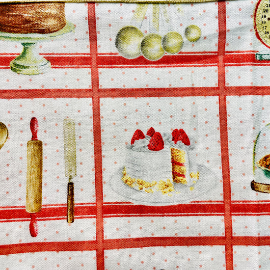 Amanda Bright Designs white baking apron with a red checkered pattern featuring illustrations of baking-related items like a cake, pie, and rolling pin domed cupcakes with canvas pockets and cotton strings