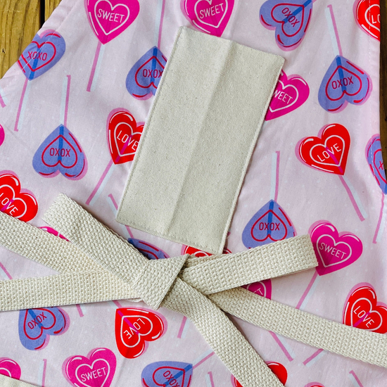 amanda bright designs 100% cotton original design heart lollipop apron Valentine's Day heart pattern, featuring red, pink, and purple heart lollipops with 'CUPID', 'LOVE', and 'SWEET' printed inside