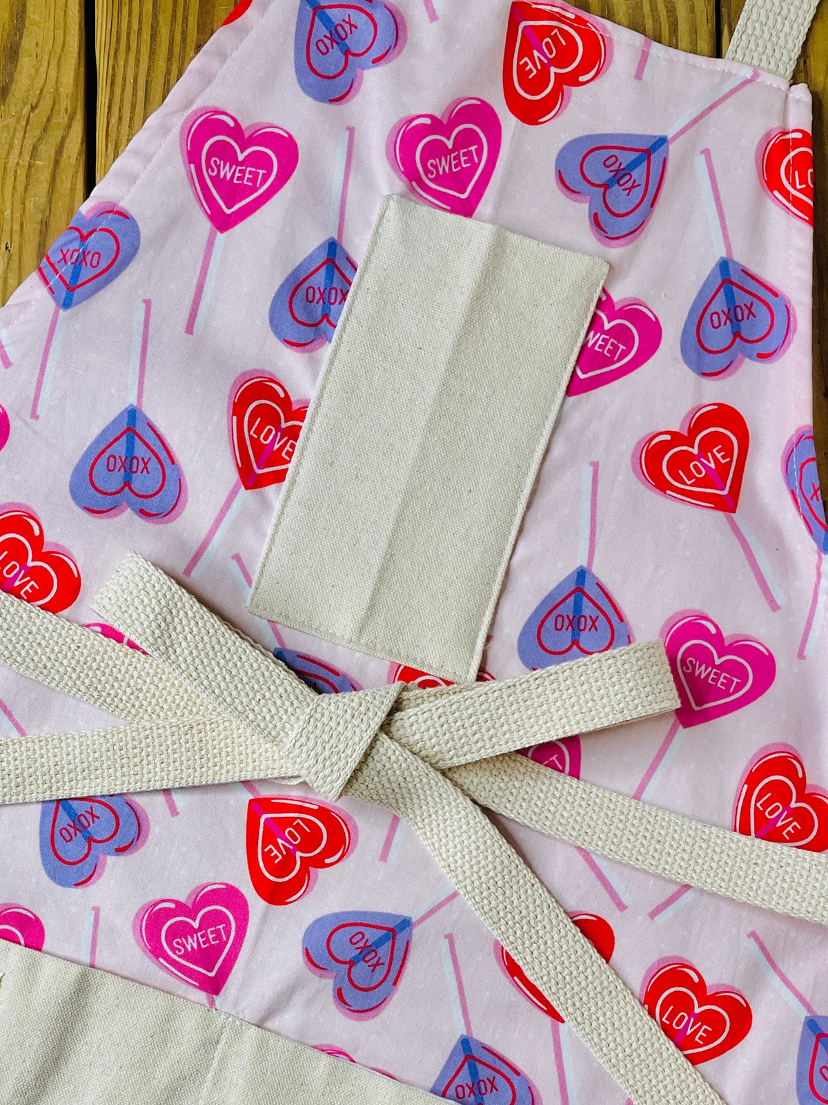 amanda bright designs 100% cotton original design heart lollipop apron Valentine's Day heart pattern, featuring red, pink, and purple heart lollipops with 'CUPID', 'LOVE', and 'SWEET' printed inside