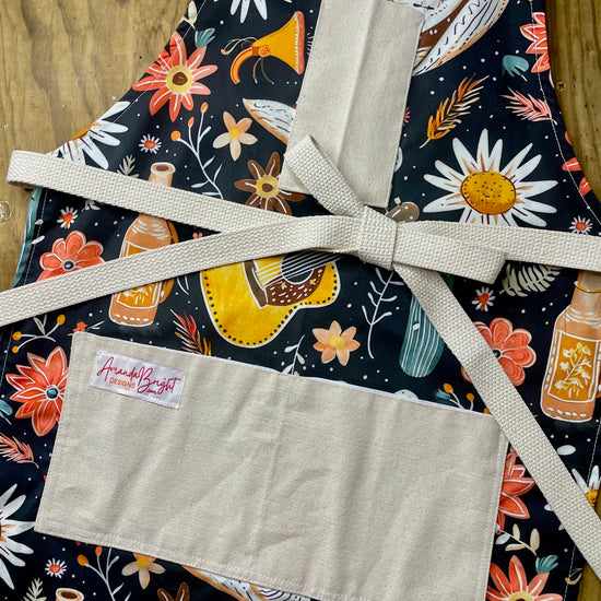 Amanda Bright Designs Delilah Apron with colorful western guitar cactus cowboy hat sunflower pattern on black background