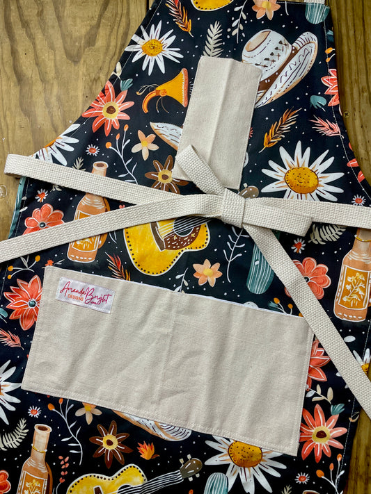 Amanda Bright Designs Delilah Apron with colorful western guitar cactus cowboy hat sunflower pattern on black background