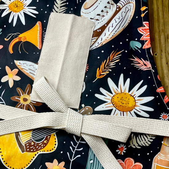 Amanda Bright Designs Desert Cowgirl Apron with colorful western guitar cactus cowboy hat sunflower pattern on black background