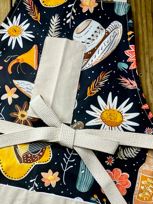 Amanda Bright Designs Desert Cowgirl Apron with colorful western guitar cactus cowboy hat sunflower pattern on black background