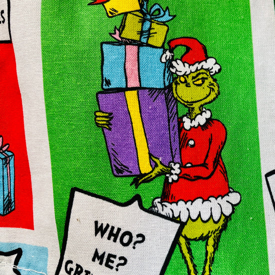 closeup of Fabric with Grinch Christmas-themed design featuring colorful presents and text.