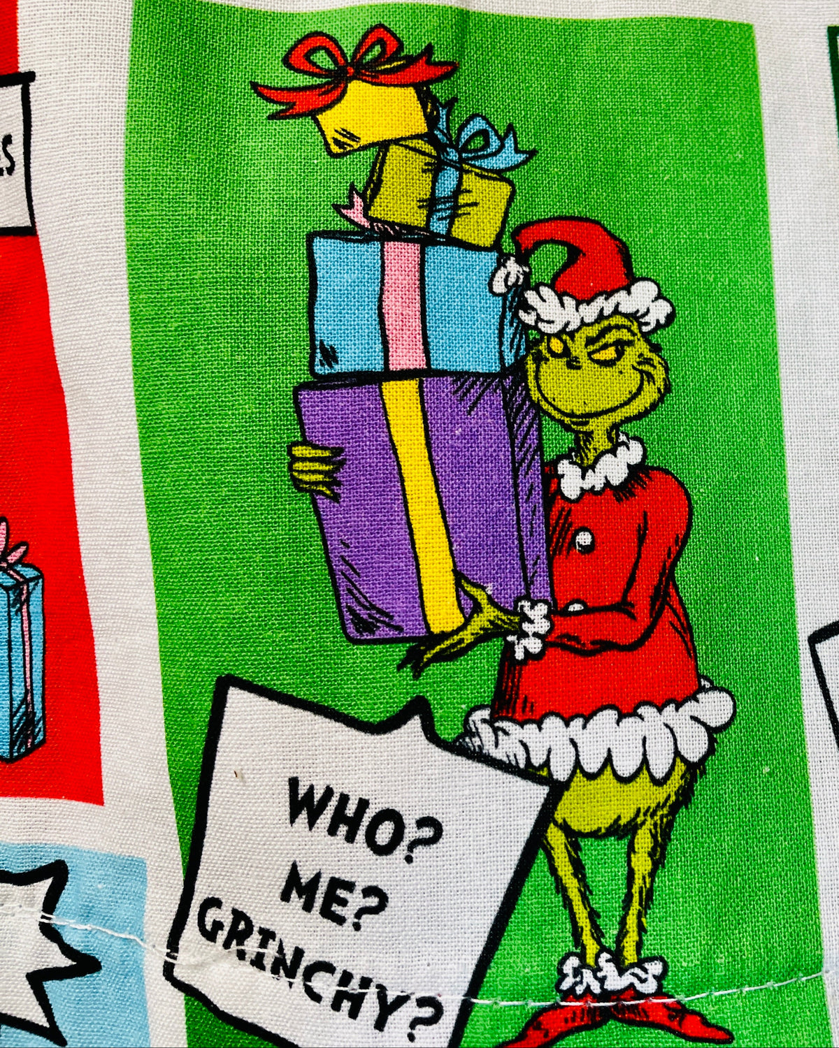 closeup of Fabric with Grinch Christmas-themed design featuring colorful presents and text.