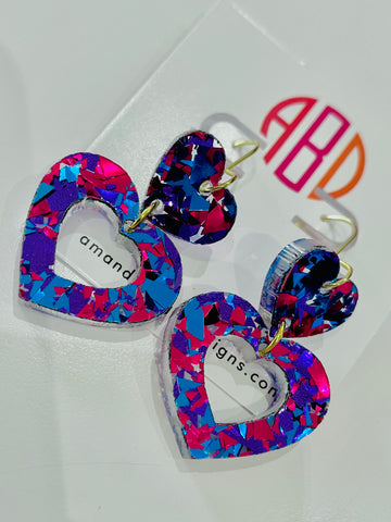 Amanda Bright Designs USA made pair of heart-shaped acrylic dangle earrings with a vibrant multicolor confetti pattern in pink, blue, and purple, featuring gold-tone hooks.