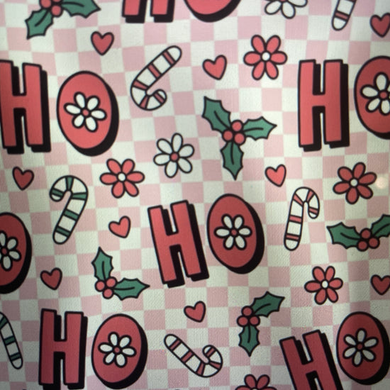 Patterned fabric with 'HO HO HO' text, candy canes, flowers, and holly leaves on a checkered background Amanda Bright Designs Couture Apron