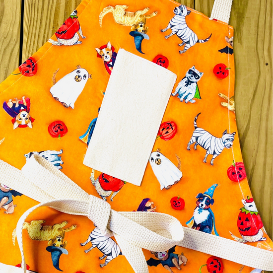 Amanda bright designs orange apron with a Halloween-themed print featuring dogs in costumes: ghosts, pumpkins, vampires and witches