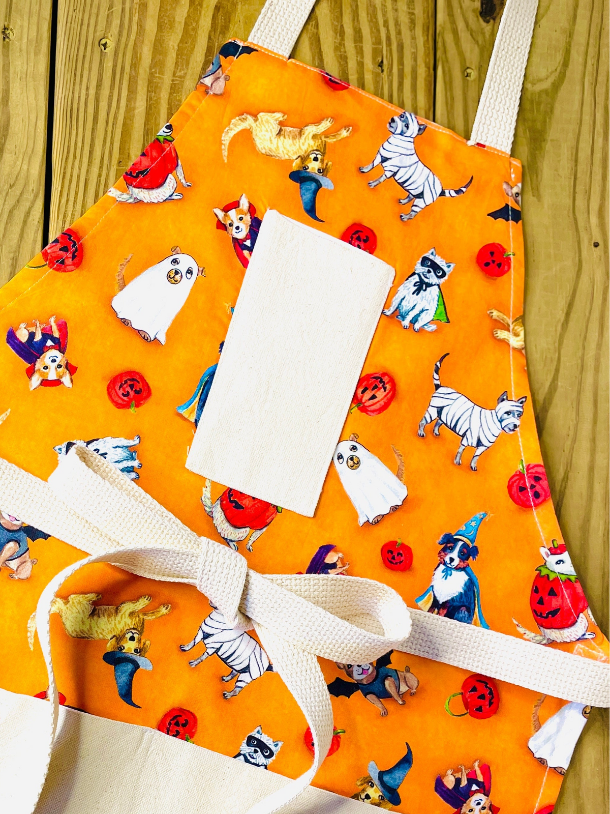 Amanda bright designs orange apron with a Halloween-themed print featuring dogs in costumes: ghosts, pumpkins, vampires and witches