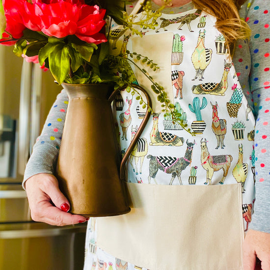amanda bright designs isabella llama flowering cactus southwest theme apron on model in kitchen holding copper pitcher wtih flowers