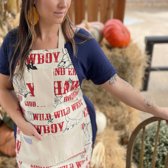 Woman wearing a cowboy-themed apron outdoors with hay bales and pumpkins in the background