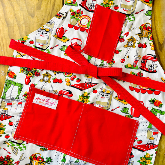 Amanda Bright Designs Lucille apron 1950s kitchen appliances pattern in red and green with red pockets and strings 