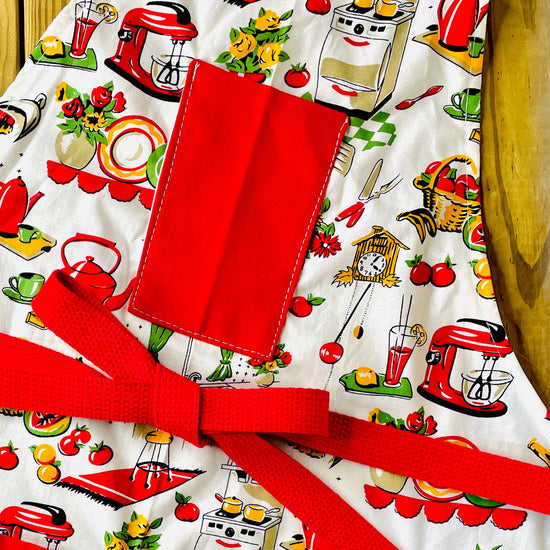 Amanda Bright Designs Lucille apron 1950s kitchen appliances pattern in red and green with red pockets and strings 