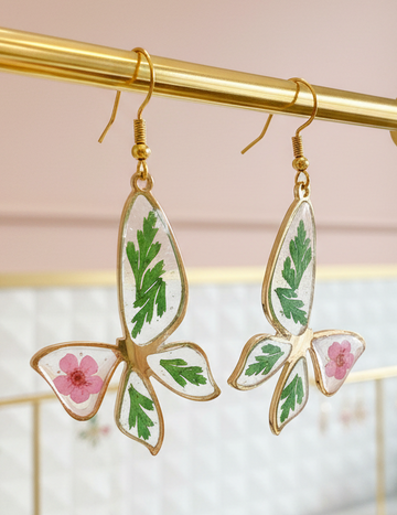 Butterfly-shaped earrings with floral designs on a gold stand against a blurred background