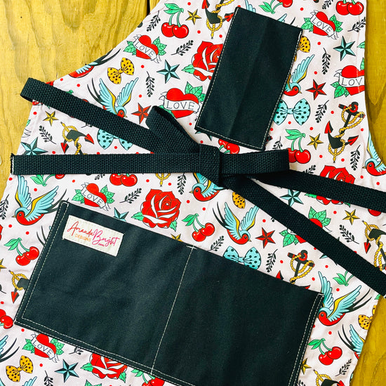 Amanda Bright Designs colorful tattoo-style nautical print of cherries, roses, stars, anchors and birds on a blush pink background with black pockets and black strings