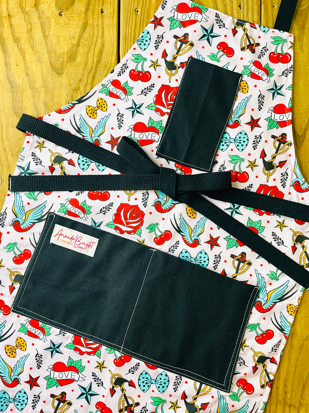 Amanda Bright Designs colorful tattoo-style nautical print of cherries, roses, stars, anchors and birds on a blush pink background with black pockets and black strings