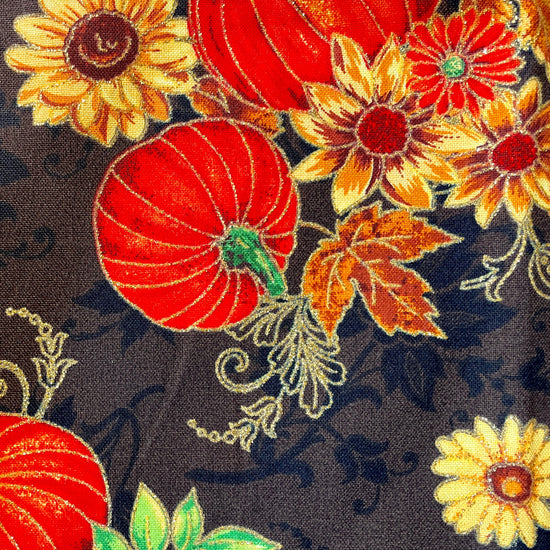 Amanda Bright Designs apron Fabric with autumn-themed design featuring pumpkins, flowers, and leaves on a brown background.