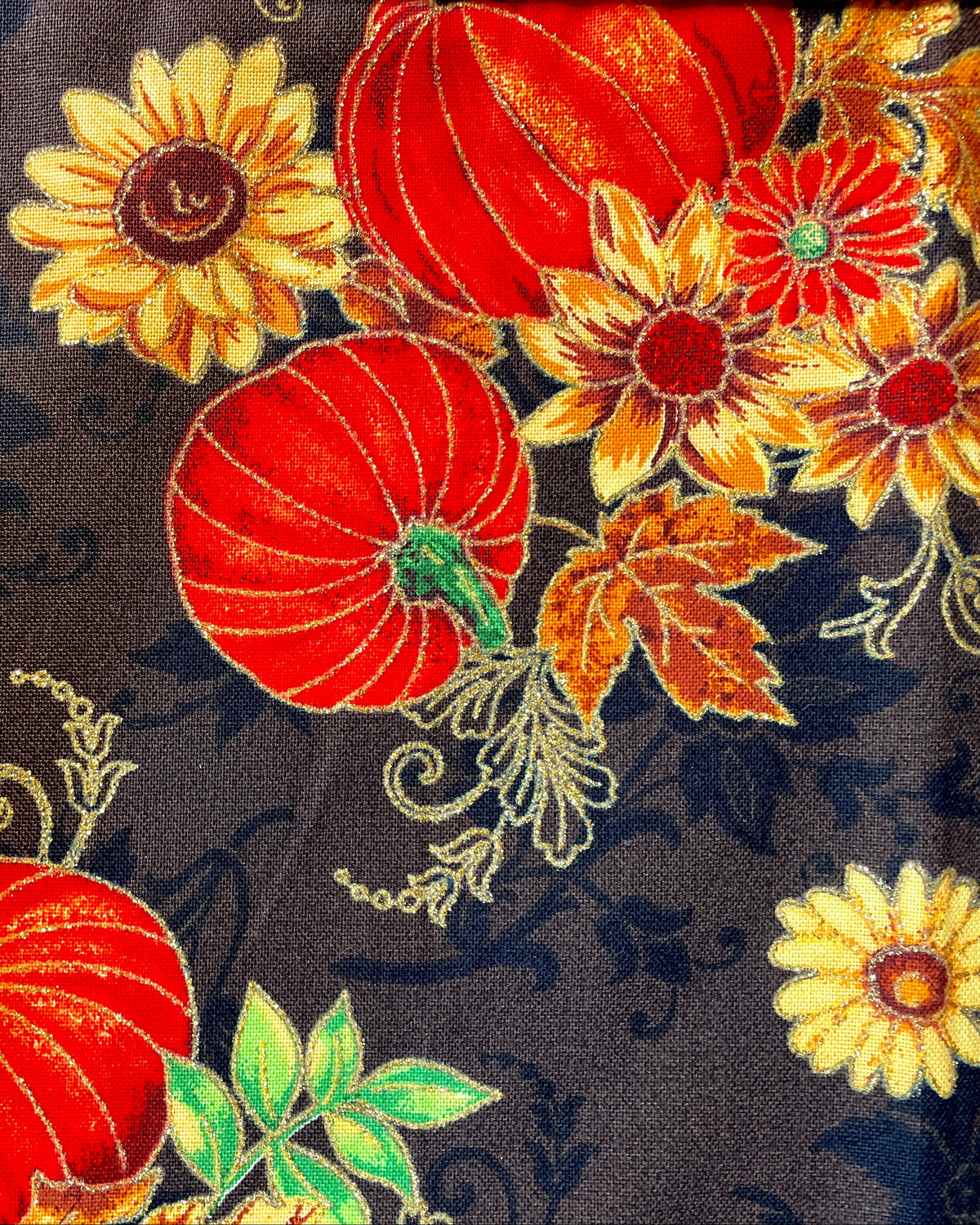 Amanda Bright Designs apron Fabric with autumn-themed design featuring pumpkins, flowers, and leaves on a brown background.