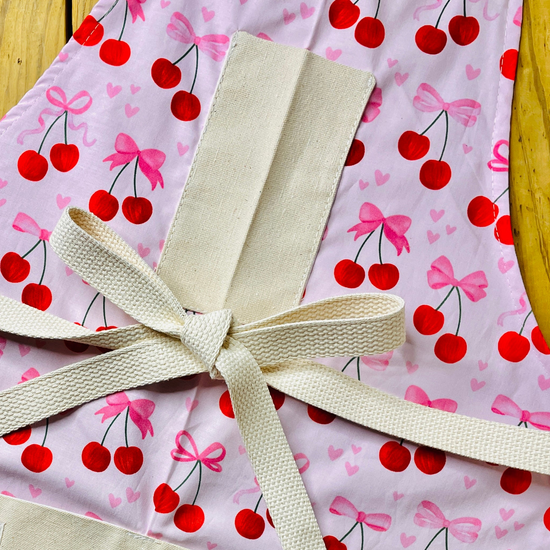 amanda bright designs close-up of a light pink apron with a repeating cherry and bow pattern motif