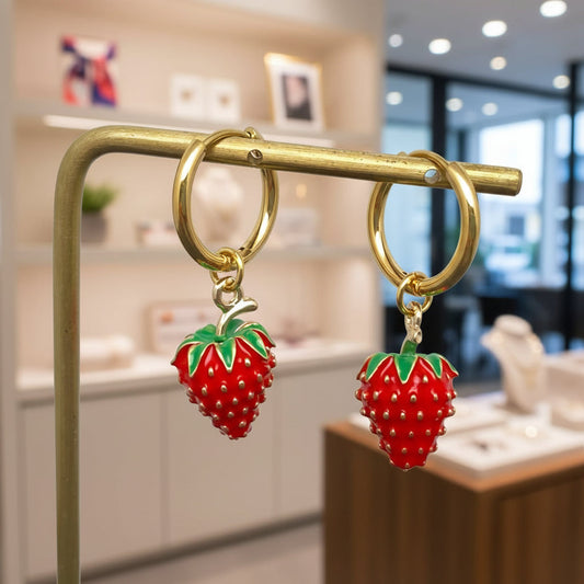 Amanda Bright Designs Gold hoop earrings with strawberry charms on a gold stand in a store setting.