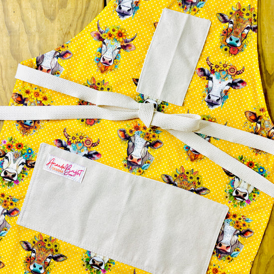 Amanda Bright Designs hand drawn cows heads with sunflowers and daisies on golden yellow polkadot background couture designer apron