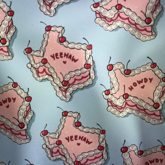 Pink Texas Shaped Iced Cakes with frosting and cherries on a light blue backgroun Amanda Bright Designs Couture Apron Collection