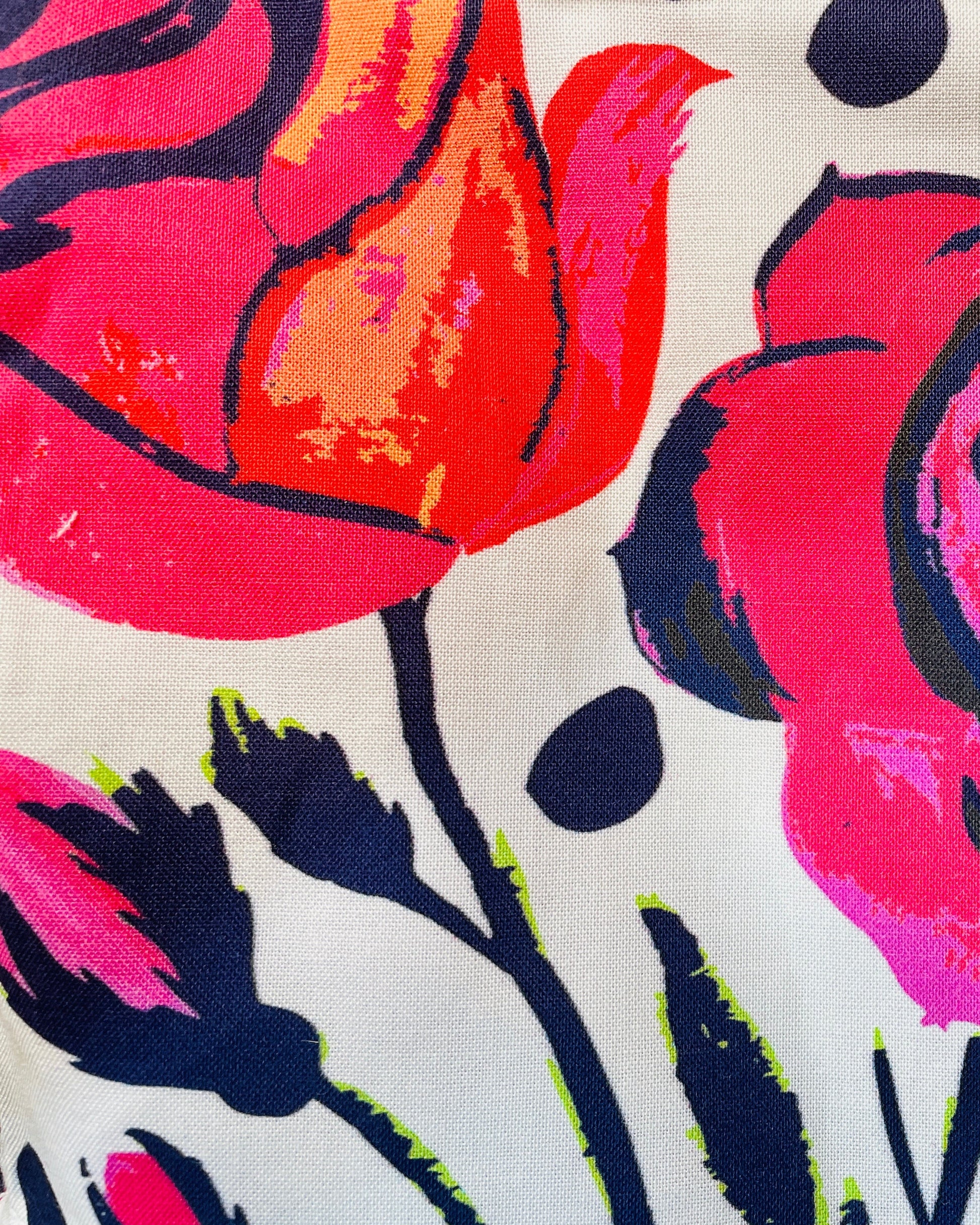 Amanda Bright Designs apron pattern Close-up of a fabric with colorful floral pattern featuring pink, red, and black roses on a white background