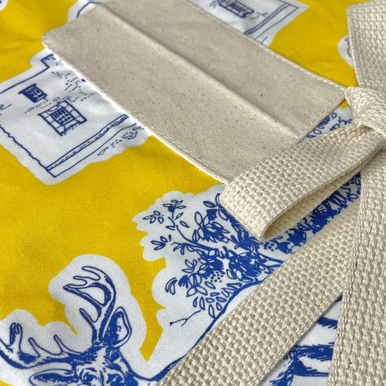 Amanda Bright Designs Texas Toile Apron feaures cowboy boots deer cactus the alamo roses in blue and white on gold background
