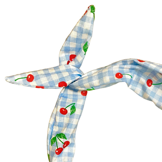 A light blue and white gingham headband with a red cherry and green leaf pattern