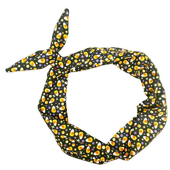 Amanda bright designs halloween fabric headband with a black background and a repeating pattern of orange, yellow, and white candy corn, purple and yellow dots and green and purple spiders tied in a knot