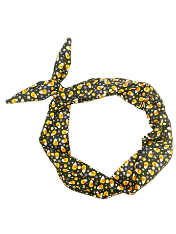Amanda bright designs halloween fabric headband with a black background and a repeating pattern of orange, yellow, and white candy corn, purple and yellow dots and green and purple spiders tied in a knot