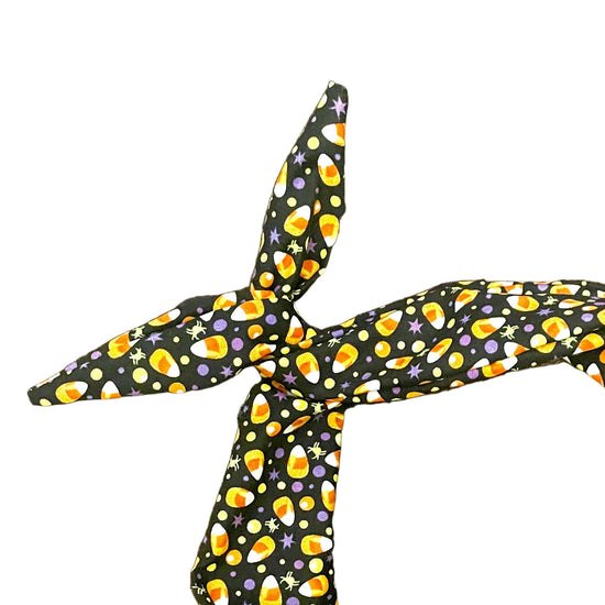 Amanda Bright Designs Halloween fabric headband with a black background and a repeating pattern of orange, yellow, and purple candy corn, tied in a knot 