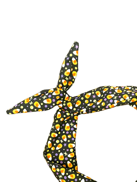 Amanda Bright Designs Halloween fabric headband with a black background and a repeating pattern of orange, yellow, and purple candy corn, tied in a knot 