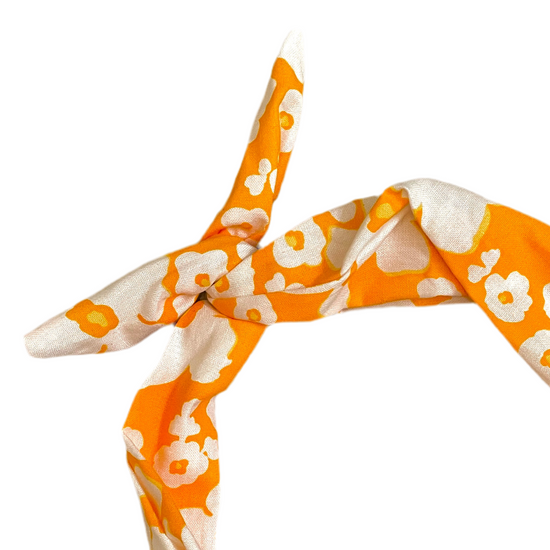 A close-up of a knotted scarf or headband featuring a bold orange and white floral pattern amanda bright designs