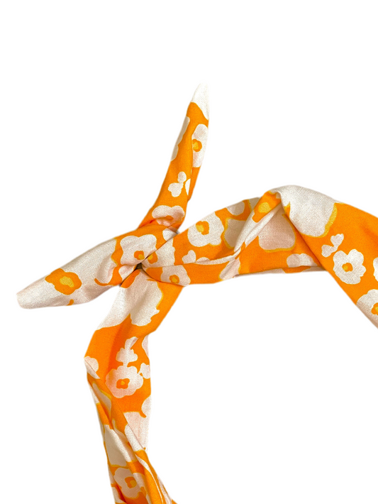 A close-up of a knotted scarf or headband featuring a bold orange and white floral pattern amanda bright designs