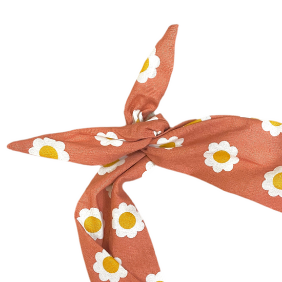 Amanda Bright Designs terracotta orange moldable cotton tie headband with a white and yellow daisy pattern, tied in a knot against a solid white background.