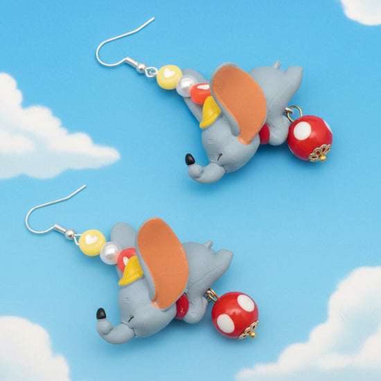 Dumbo-themed earrings on a blue background with clouds