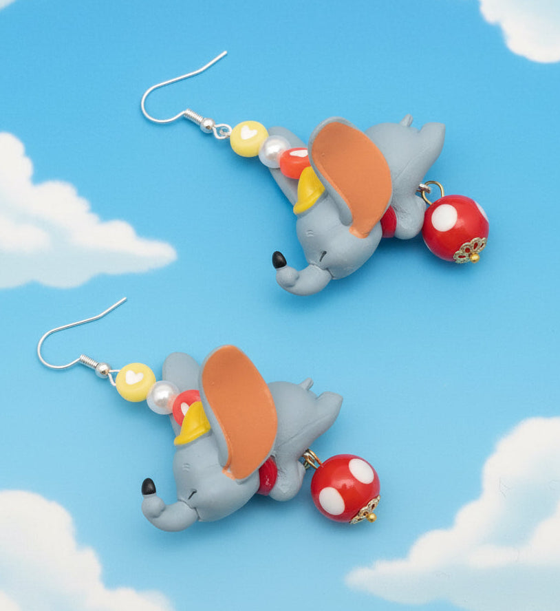 Dumbo-themed earrings on a blue background with clouds