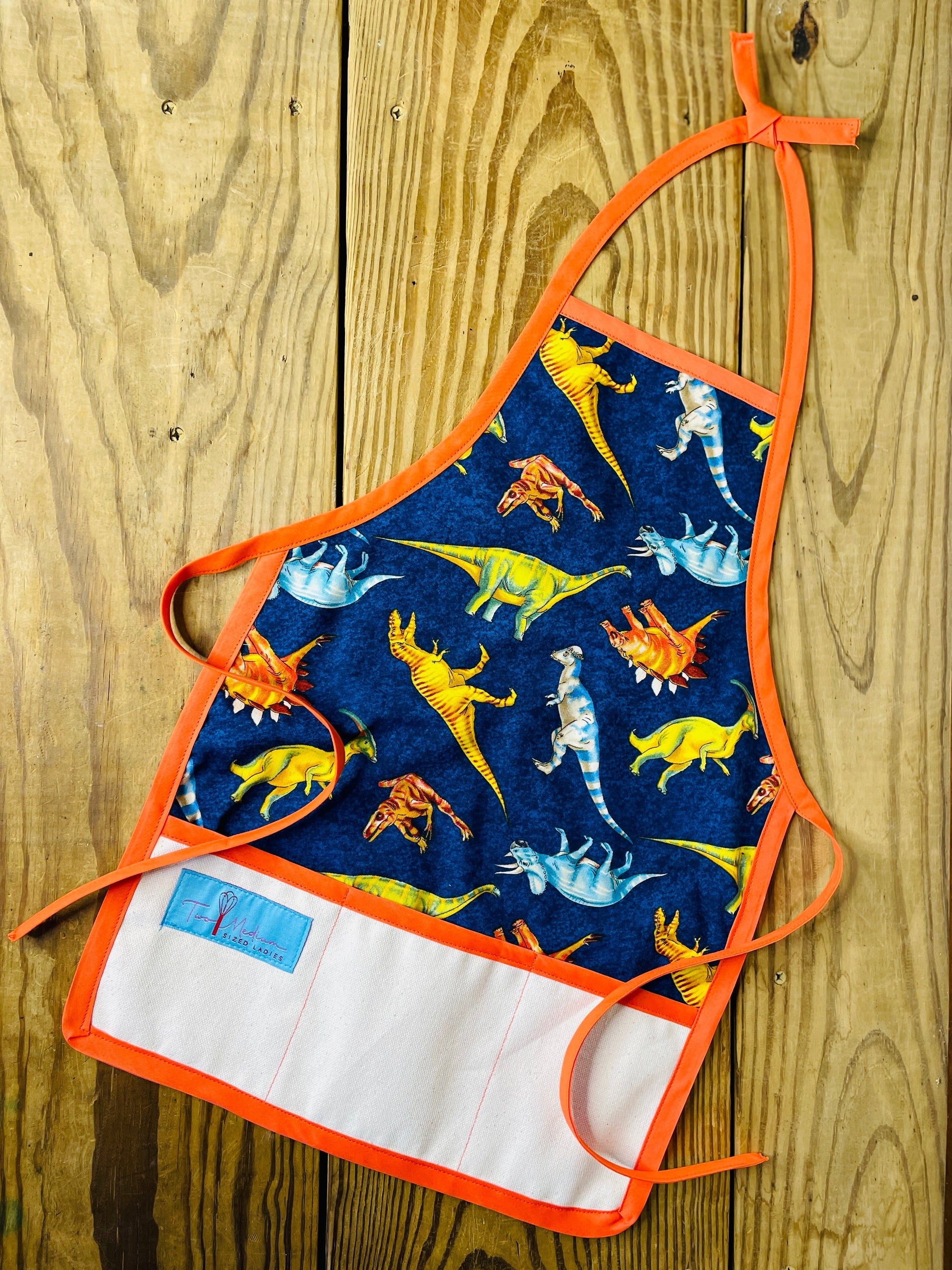 Two Medium Sized Ladies childrens dinosaur tyrannosaurus stegosaurus play time bake time apron orange strings trim